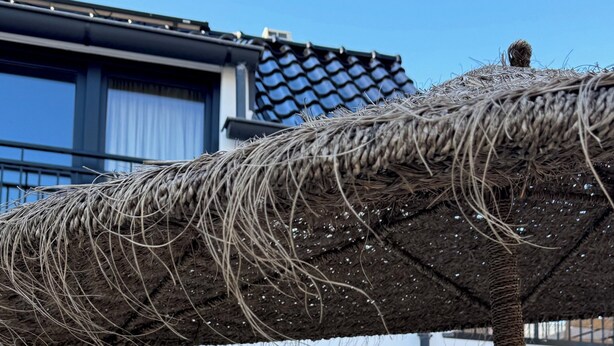 Une structure en forme de parasol recouverte de chaume, un bâtiment moderne doté de grandes fenêtres et des espaces de repos en plein air.