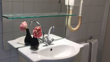 Un baño con lavamanos blanco, estante de vidrio, espejo y toallero.