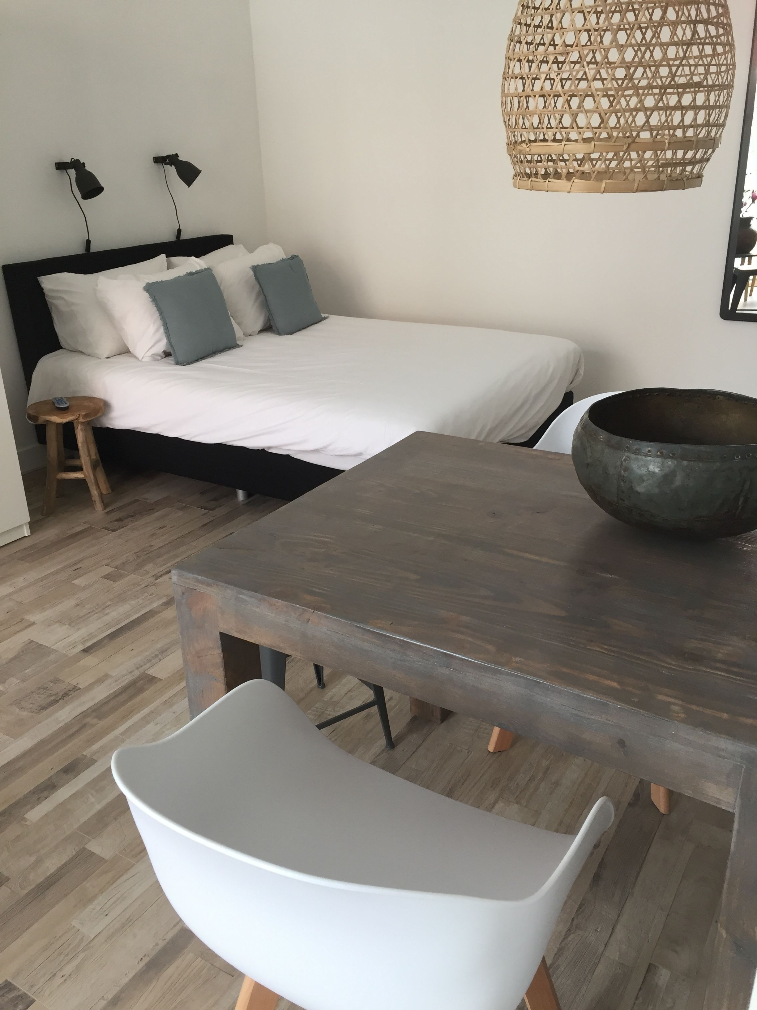 A bedroom with a bed, bedside lamps, a bedside table, a chair, and a hanging light fixture.