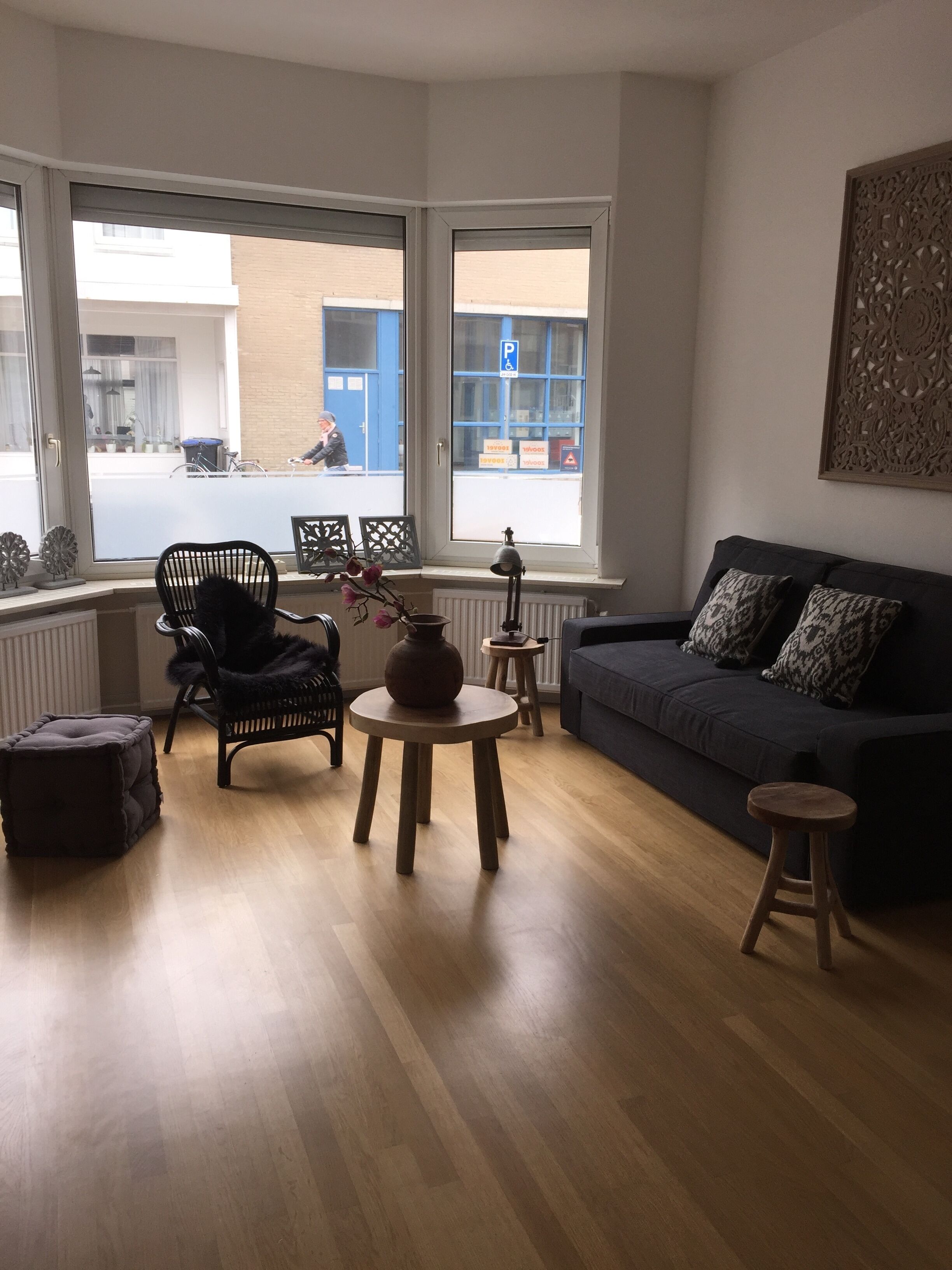 Un salon comprenant un canapé, un fauteuil, une petite table et une fenêtre donnant sur la rue.