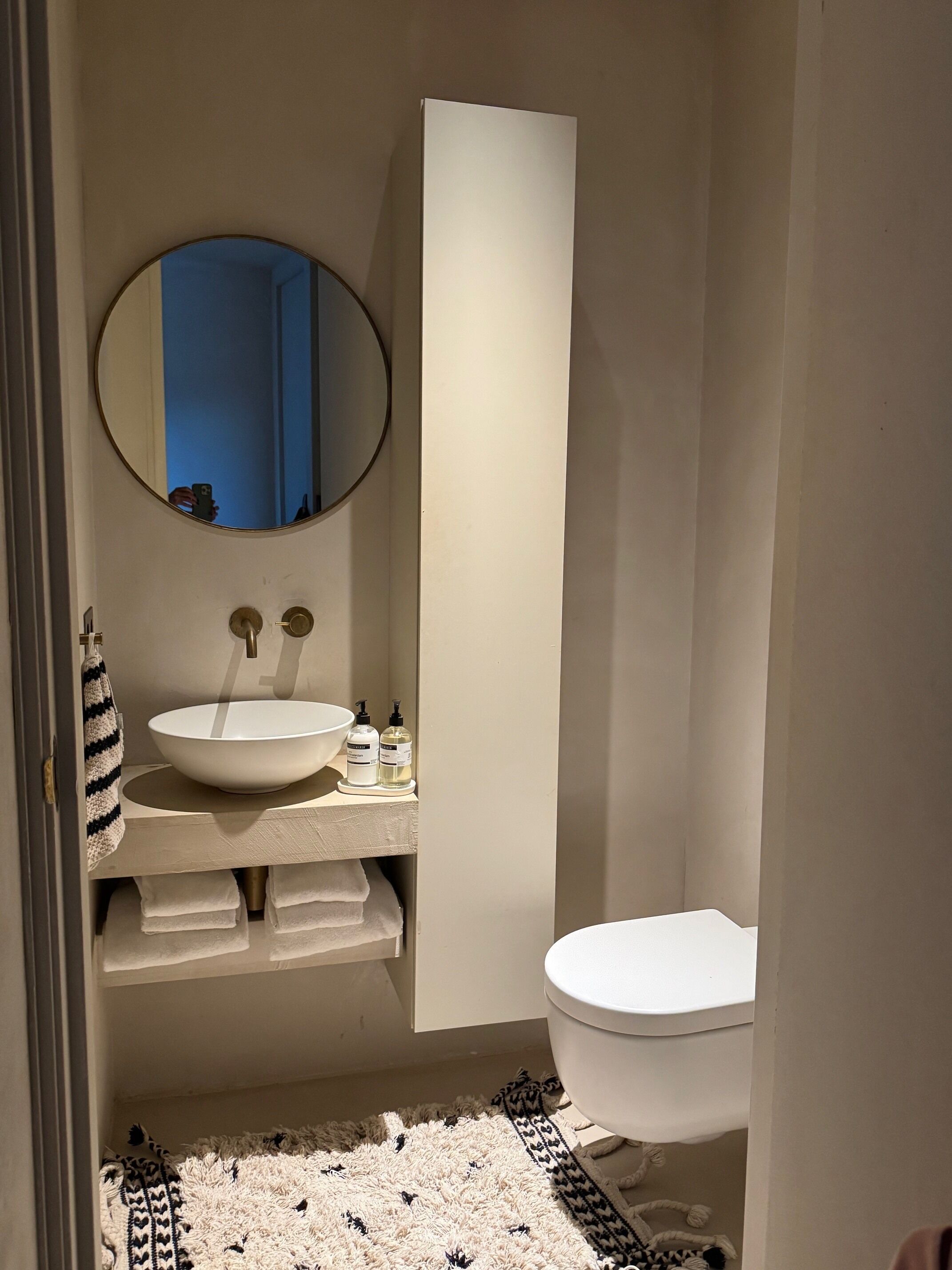 A bathroom with a round mirror, a white sink, and a toilet.