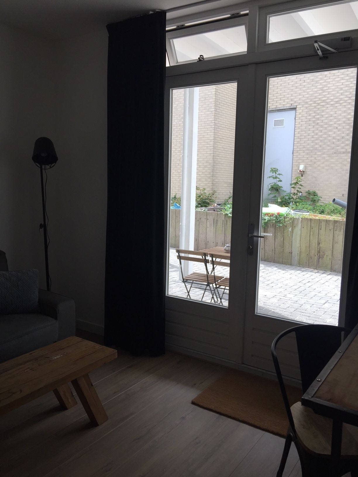Une pièce dotée d’une grande porte-fenêtre coulissante qui donne sur un patio. On y trouve une table en bois et une chaise, et une lampe sur pied est visible à l’intérieur de la pièce.