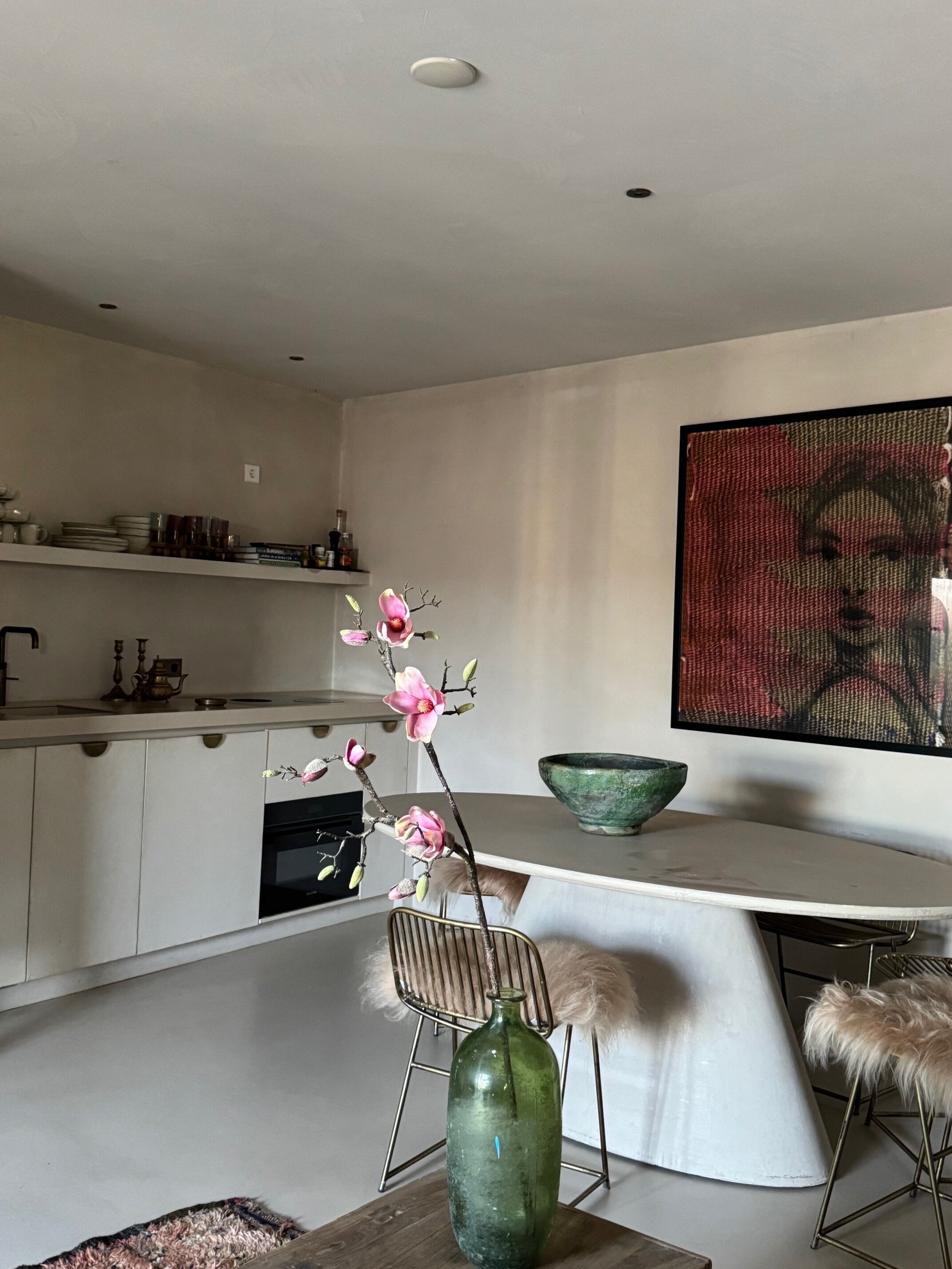 Una cocina moderna con armarios blancos, un jarrón verde con flores y un cuadro grande en la pared.