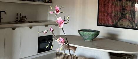 A modern kitchen with white cabinets, a green vase with flowers, and a large painting on the wall.