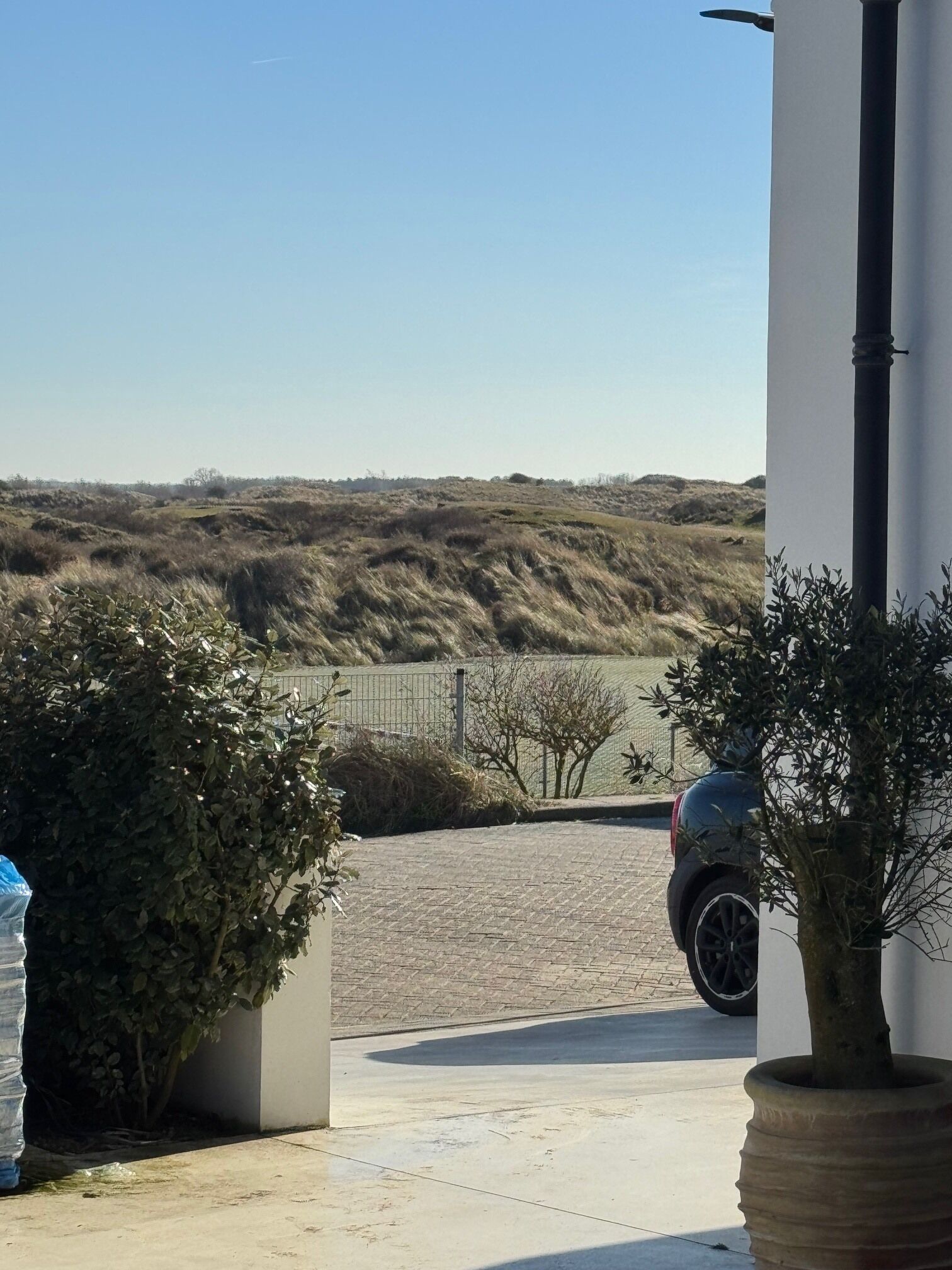 A paved driveway leading to a vehicle parked near a white building with a view of a hilly landscape.