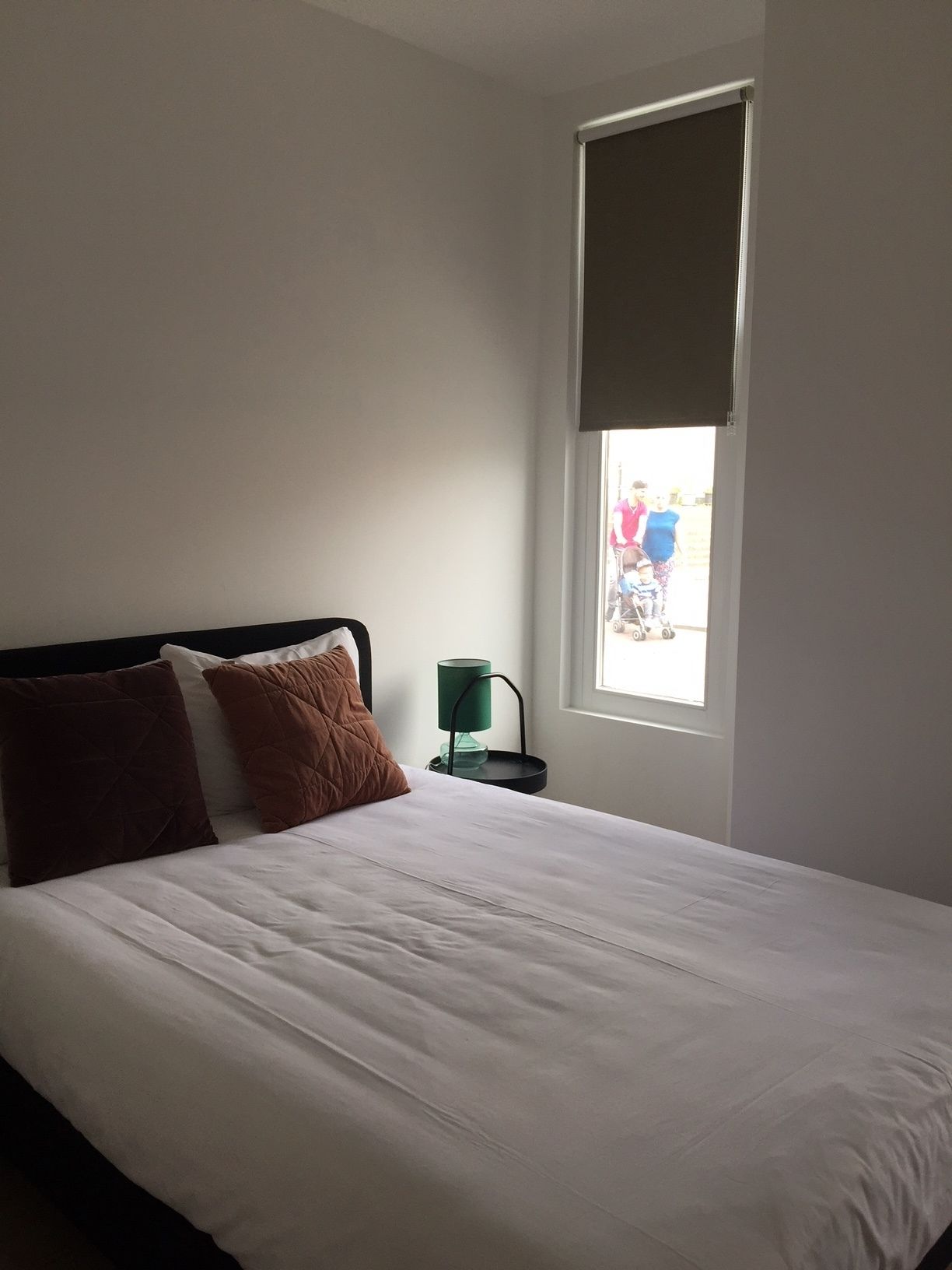 Une chambre à coucher avec un lit, des oreillers, une table de chevet, une lampe et une fenêtre.