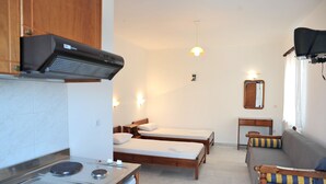A compact hotel room with a kitchenette, two single beds, a sofa, and a mirror. - Helios Beach Studios (Naxos)