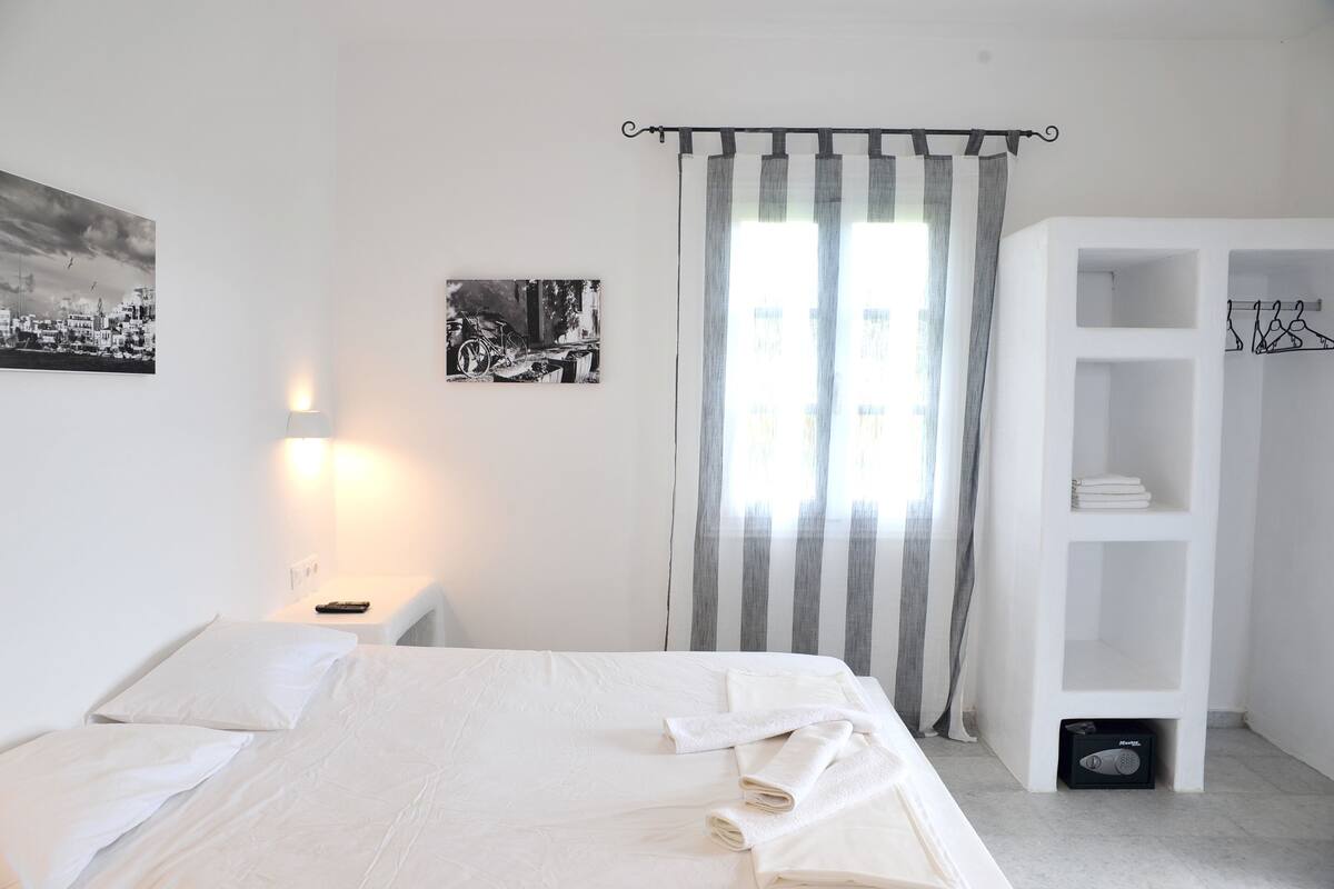 A bedroom with a bed, a nightstand, a lamp, a wardrobe, and two framed pictures on the wall.