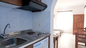 A kitchen with a built-in stove, sink, and ventilation hood. There is a wooden dining table and chairs in the adjacent dining area. - Helios Beach Studios (Naxos)