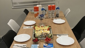 Una larga mesa dispuesta para una comida, con platos, cubiertos y una variedad de alimentos, incluyendo pan, huevos y una ensalada.