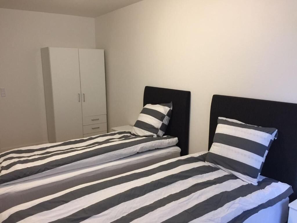Camera da letto con due letti, ognuno con biancheria a righe, un armadio bianco e una testiera nera.