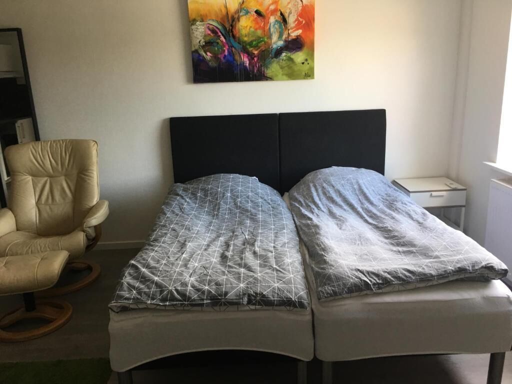Un lit simple avec une tête de lit noire, une chaise et un tableau accroché au mur.