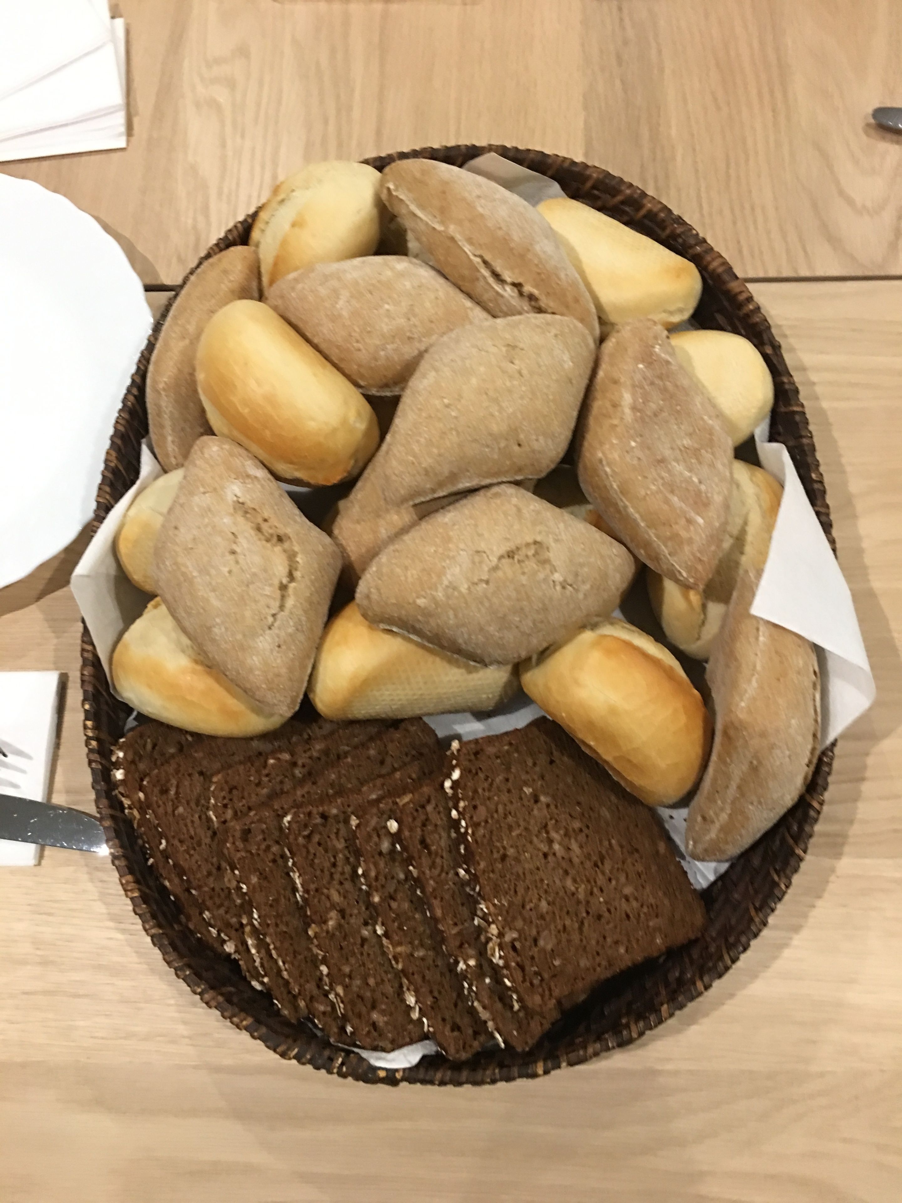 Una cesta con panecillos variados y una hogaza de pan oscuro sobre una mesa de madera.
