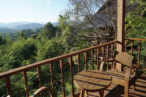 A wooden deck with a table and chairs, overlooking a lush green landscape and distant mountains. - Thanyarat Resort and Organic Farm (Mae Rim)