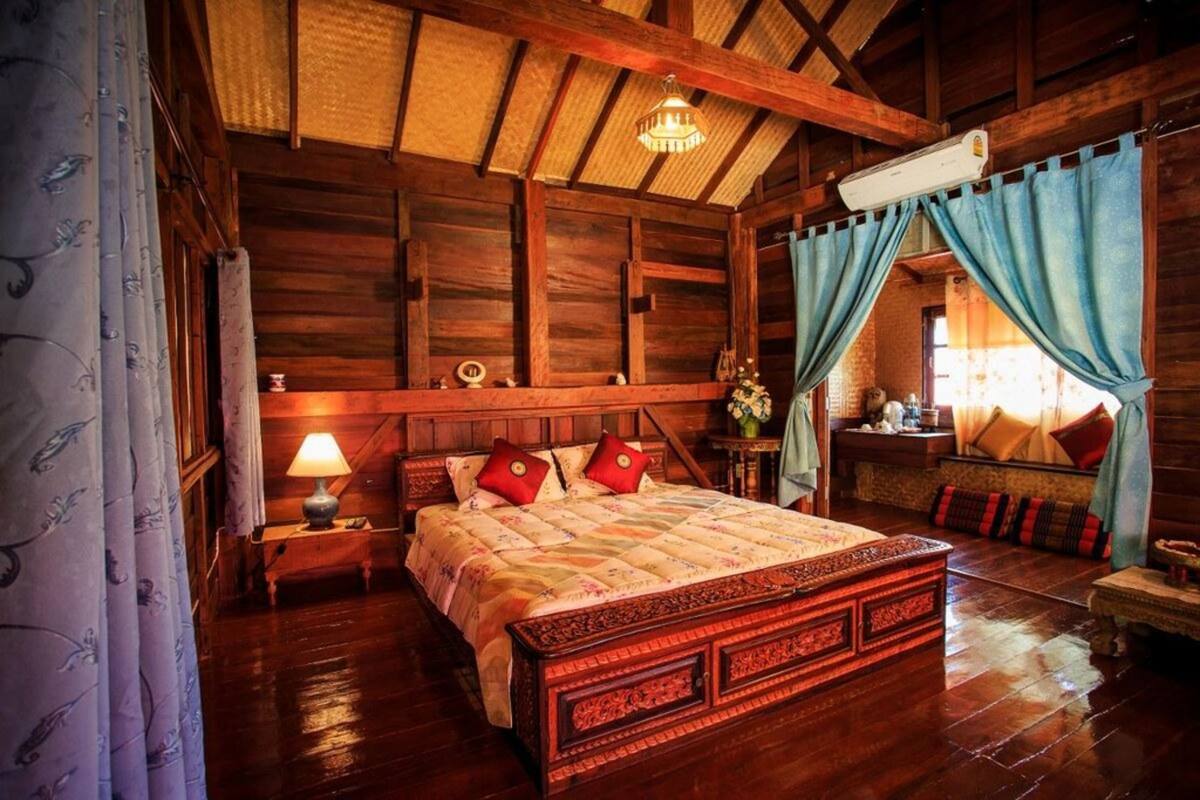 Una habitación de madera con una cama, una mesita de noche, una lámpara y una ventana con cortinas.