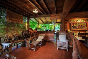 A rustic wooden interior with a wooden ceiling, a bench with animal carvings, a fan, and a painting on the wall. - Thanyarat Resort and Organic Farm (Mae Rim)