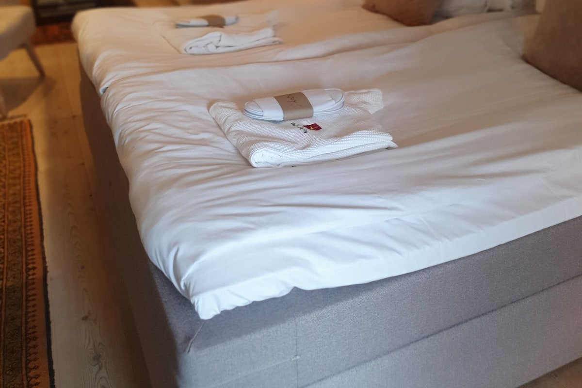 A hotel room with two beds, a wooden ceiling, a small table, and a chair.