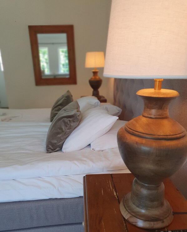 Una cama bien hecha con almohadas y una mesita de noche de madera con una lámpara.