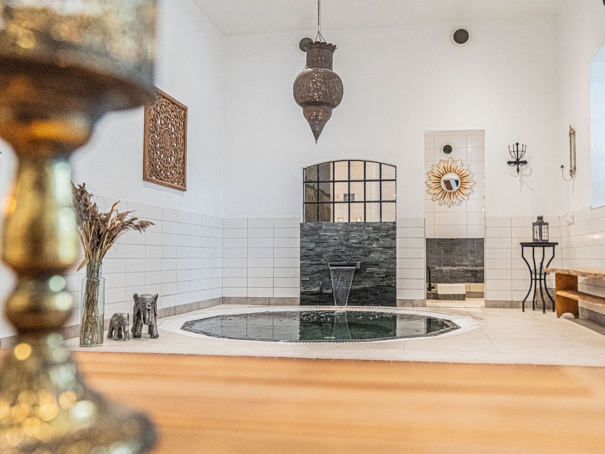 A modern bathroom with a freestanding bathtub, a decorative wall piece, and a small table with a lantern.