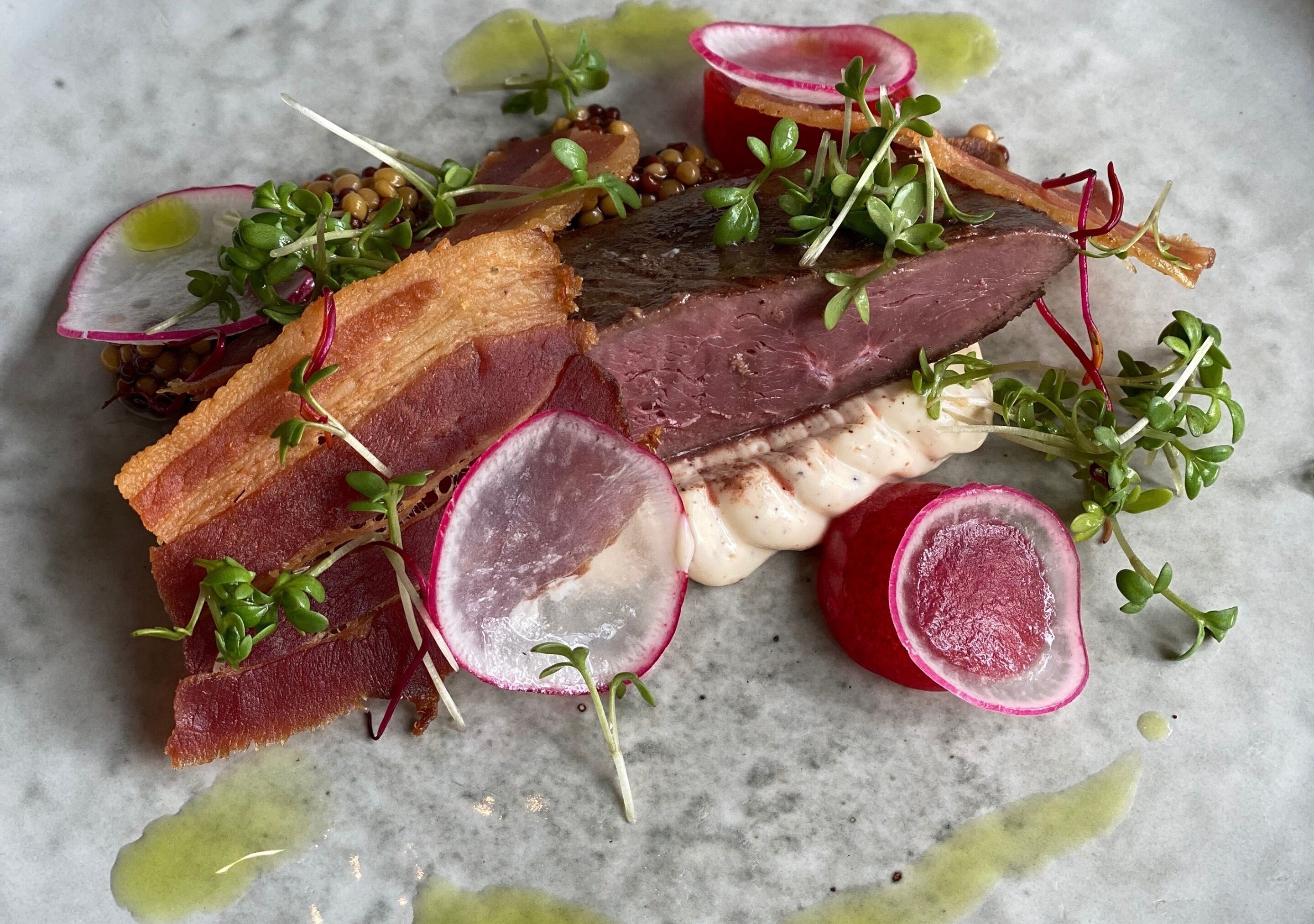 Un plato con diversas carnes y verduras sobre una superficie de mármol.