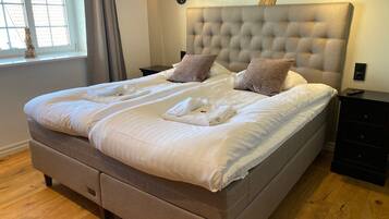 Una cama bien hecha con un cabecero capitonado, dos mesitas de noche y una ventana con cortinas.