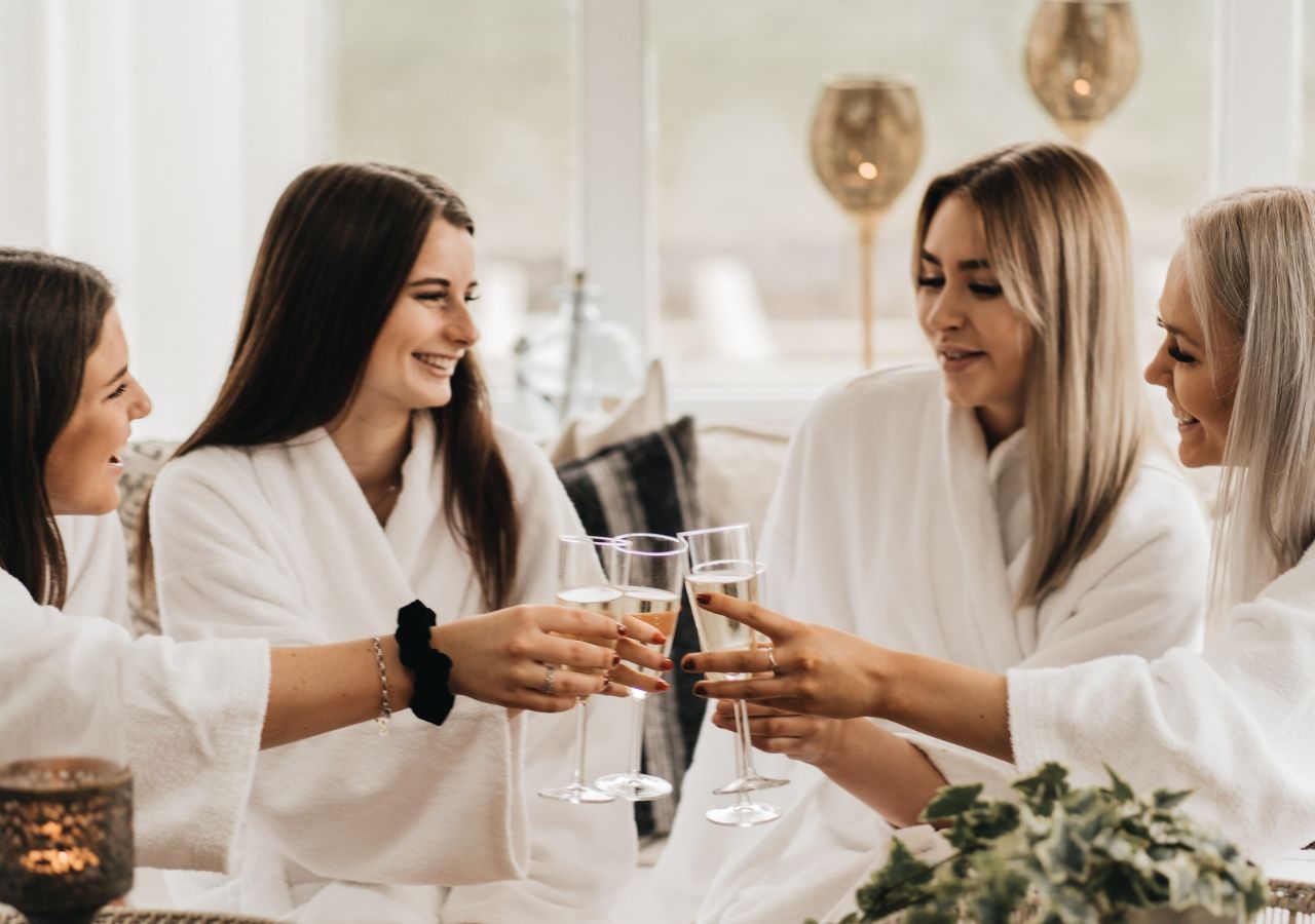 A group of people in white robes toasting with champagne glasses in a well-lit room with a modern interior.