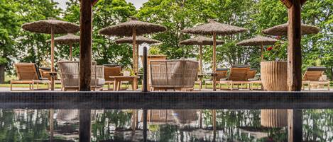 Een zwembadterras met ligbedden, parasols en een houten pergola.
