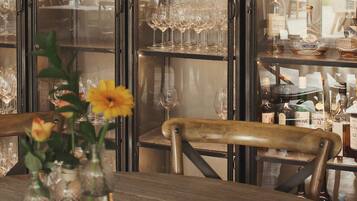 Una zona de bar con estantes llenos de copas y botellas de vino, una silla de madera y un jarrón con flores.