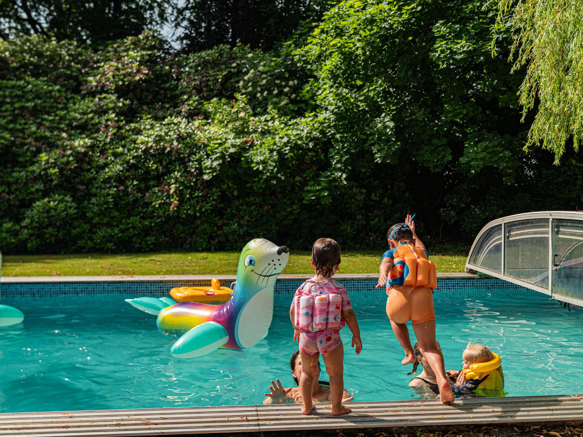 En swimmingpool med oppustelige legetøj og mennesker omkring.
