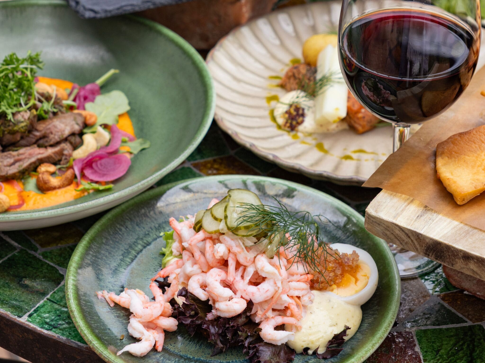 Diversos pratos com camarões, legumes e um copo de vinho tinto.