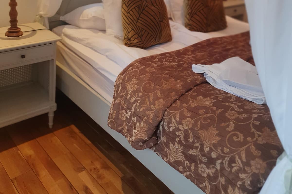 A bedroom with a four-poster bed, white bedding, and brown patterned pillows.
