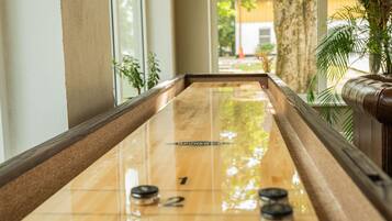 Una mesa de shuffleboard con áreas de puntuación numeradas, ubicada en un pasillo con ventanas amplias y plantas de interior.