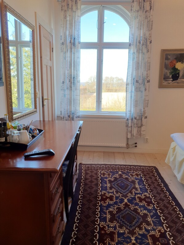 A room with a large window, a wooden dresser, a patterned rug, and a painting on the wall.