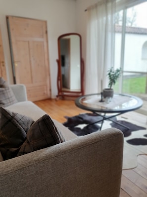 A living room with a sofa, a round coffee table, a mirror, and a view of the outdoors through large windows. - Elisefarm (Hoor)