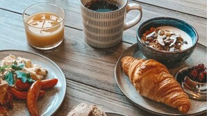 A breakfast setting with plates of food, a croissant, a coffee mug, and a bowl of cereal.