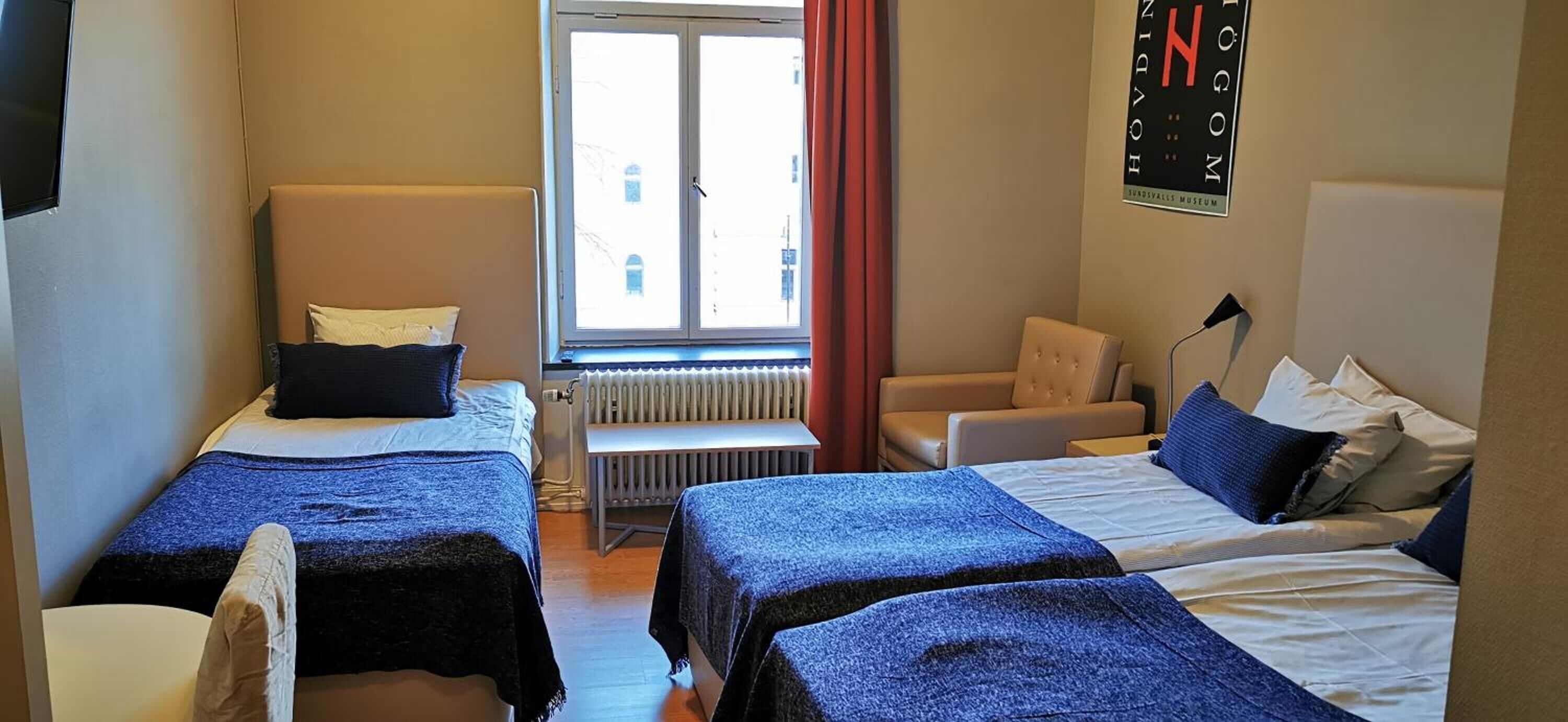 Ett hotellrum med två sängar, ett fönster med gardiner, ett element och en stol.
