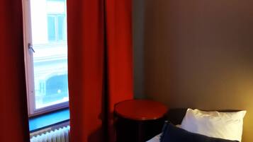 A hotel room with a bed, a small table, and a window with red curtains.