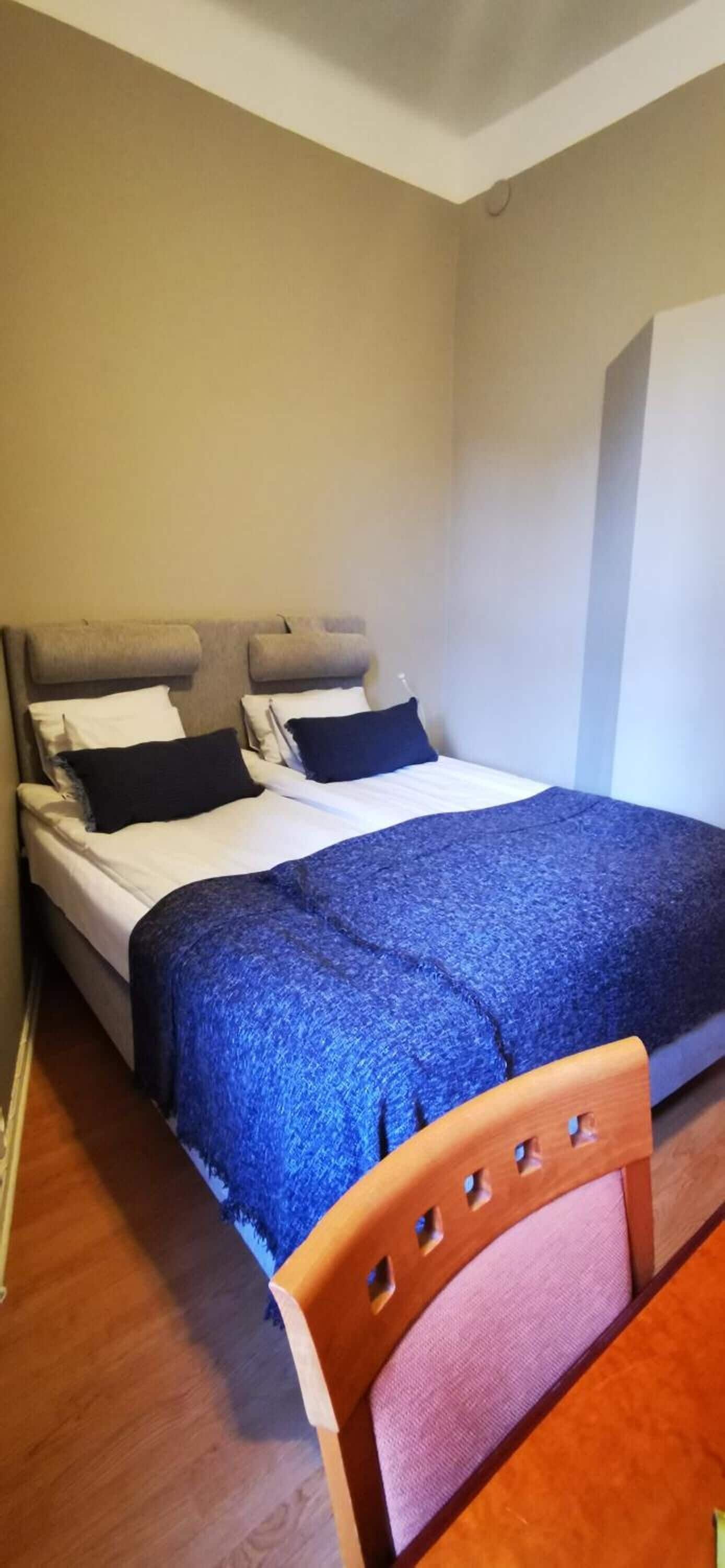 A bedroom with a bed, two pillows, a blue blanket, and a wooden chair.