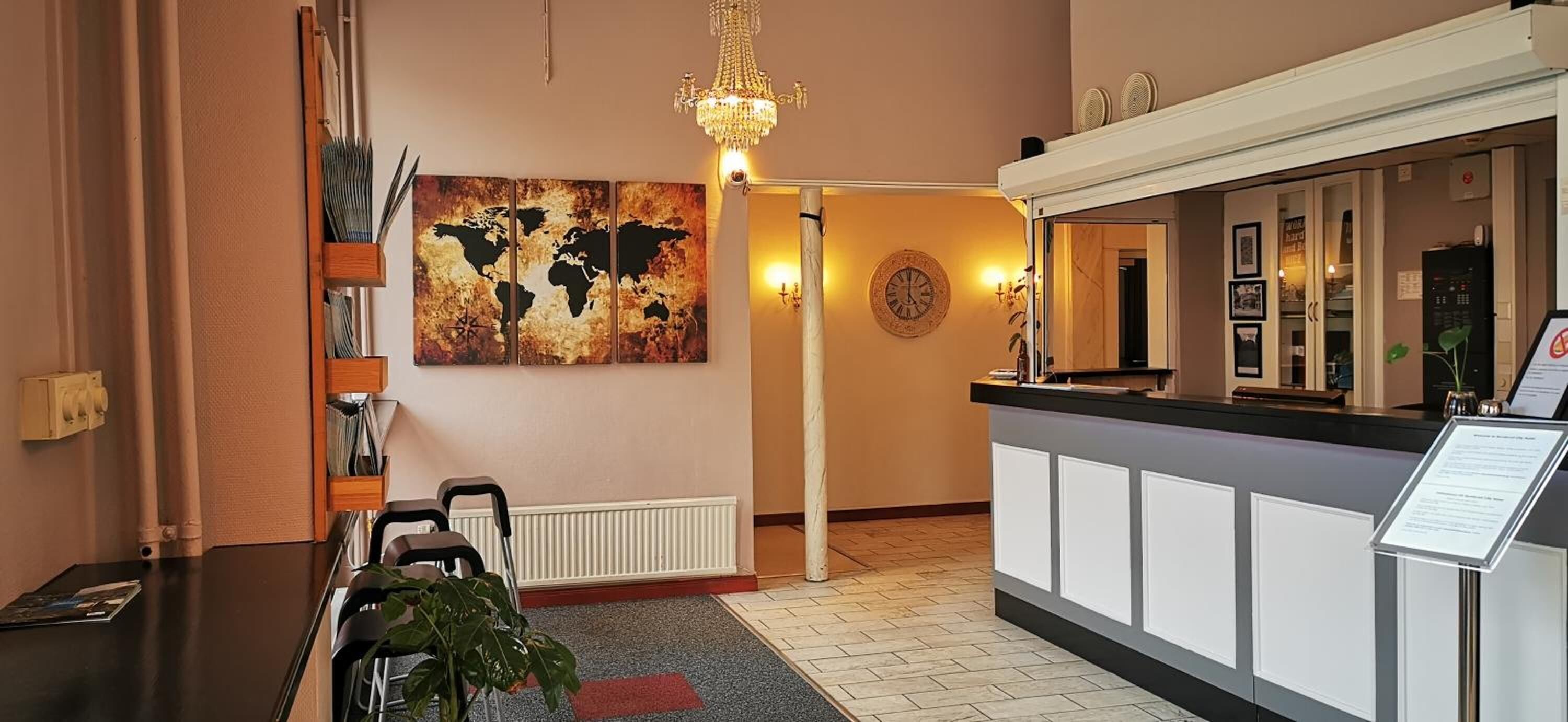 A reception area with a world map artwork, a chandelier, a reception desk, and a plant.