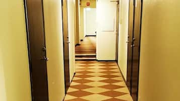 A hotel hallway with a checkered floor pattern, doors on both sides, and a light source at the end.