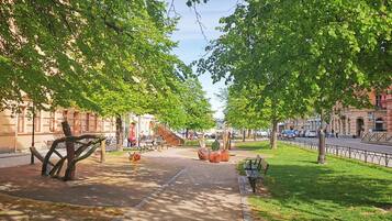 A tree-lined pedestrian path with benches, a sculpture, and a playground.