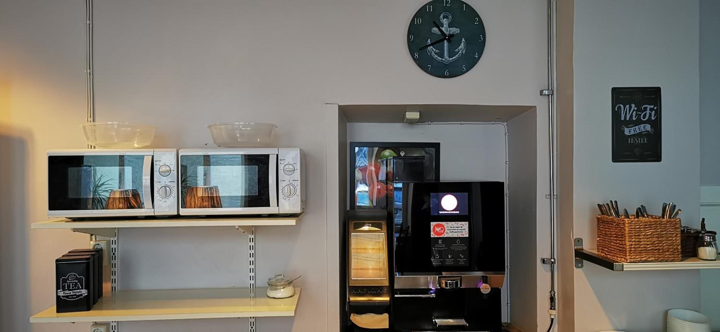 A kitchenette with a microwave, a coffee machine, and a clock on the wall.