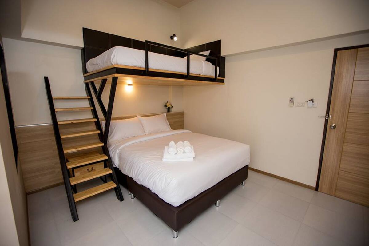 Un dormitorio con una litera, una escalera de madera, una mesita de noche y una puerta.
