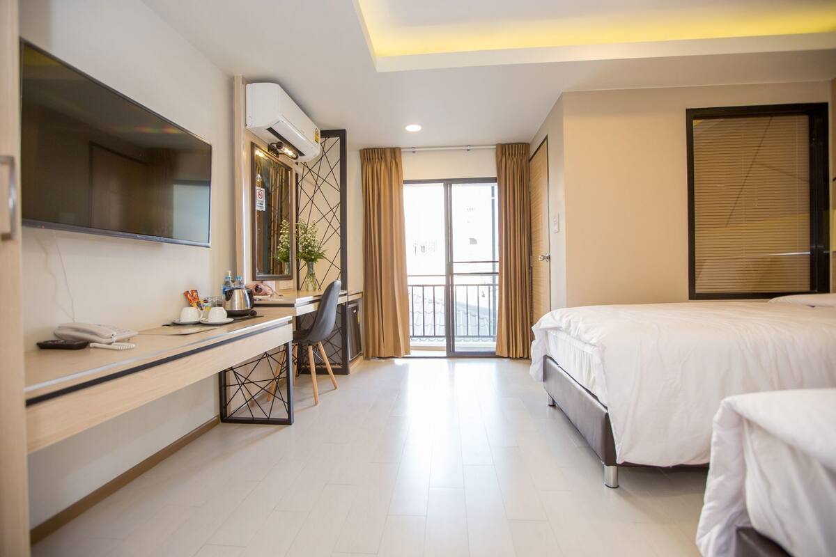 Habitación de hotel con cama, escritorio, teléfono, silla, televisor y ventana con cortinas.