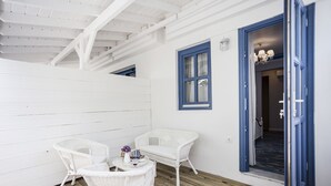 A room with white wicker furniture, a wooden floor, and a blue-framed window. - Sardunya Otel (Bozcaada)