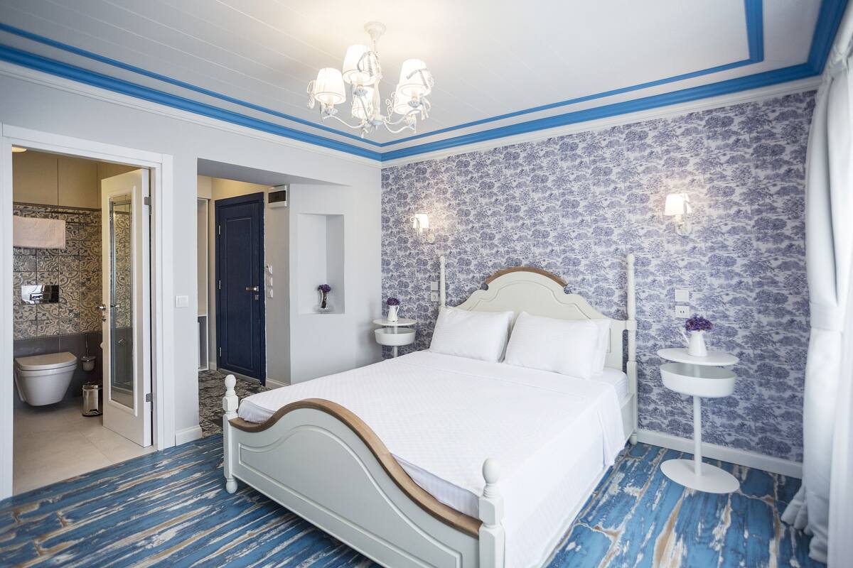 A bedroom with a bed, a nightstand, a wall-mounted light, and a bathroom visible through an open door.