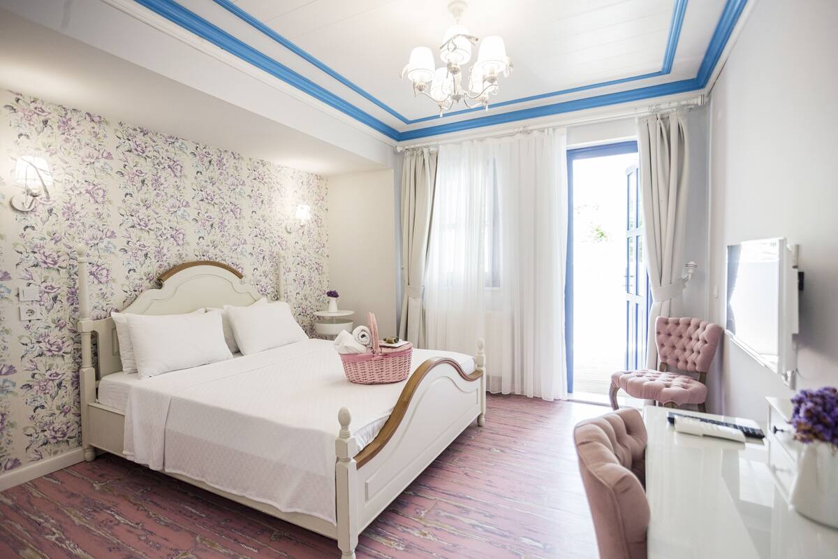A bedroom with a bed, a desk, a chair, a television, and a window with curtains.