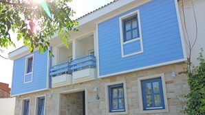 A two-story building with a blue exterior, stone facade, and a balcony. - Sardunya Otel (Bozcaada)