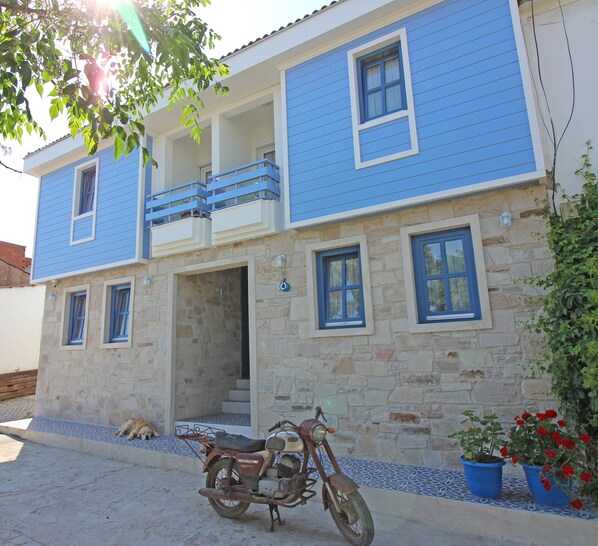 A two-story building with a blue exterior, stone facade, and a balcony. - Sardunya Otel (Bozcaada)