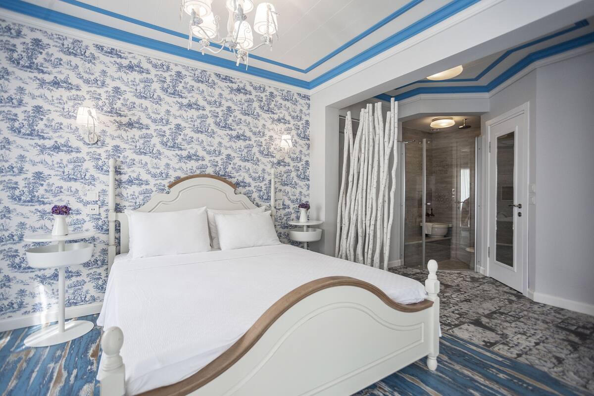A bedroom with a large bed, a bedside table, a nightstand, a shower area, and a bathroom with a toilet and sink.